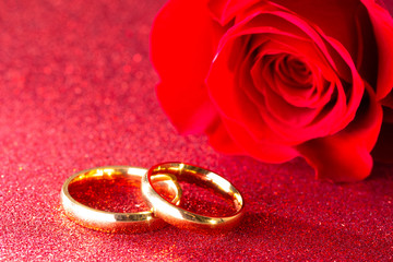 Wedding Bands and a Red Rose on a Red Glitter Background