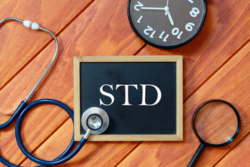 Top view of stethoscope,magnifying glass,clock and blackboard written with STD (Sexually...