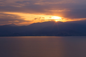 beautiful picturesque romantic sunset scenic landscape with sea calm water surface and vivid orange sun rays from above mountain ridge silhouette, post card landscape wallpaper pattern concept
