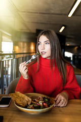 Young freelance woman is eating mixed vegetable salad in cafe