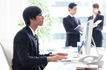 窓際の明るいデスクでパソコン業務を行う男性会社員