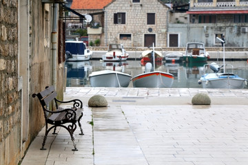Retro bench on a promenade in town Stari Grad, island Hvar, Croatia. View of sea and small fishing boats in the background. Selective focus.