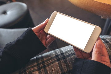 Mockup image of hands holding and using a white mobile phone with blank screen horizontally while sitting in cafe