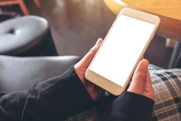 Mockup image of hands holding and using a white mobile phone with blank screen while sitting in cafe