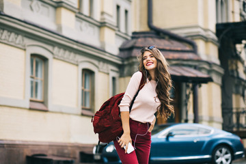 Obraz premium Cute girl with vinous bag is walking in the city. She has long hair, listening to music and smiling to side.