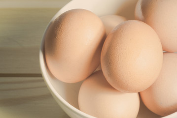 Close-up top view raw chicken eggs in a bowl on wooden table.