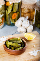 Bowl of pickled cucumbers and jars of pickled vegetables on wooden background