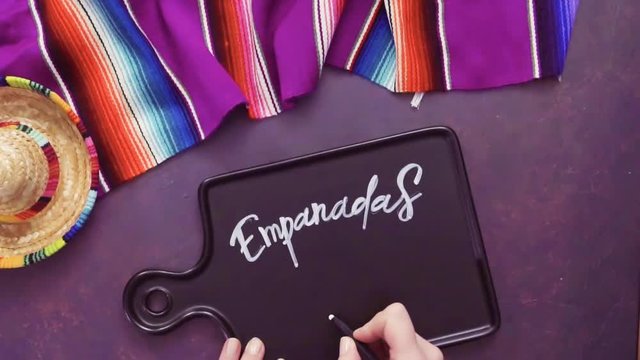 Flat lay. Writing Emapanadas sign on black chalk board.