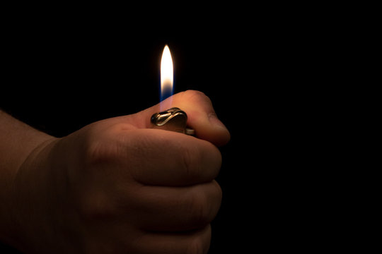 Hand illuminated by flame from lighter on a black background