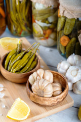 Bowl of pickled garlics and green peppers with jars of pickled vegetables on wooden background