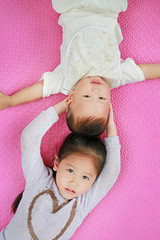Obraz na płótnie Canvas Adorable cute Asian sister and little brother lying on pink mattress mat looking at camera.