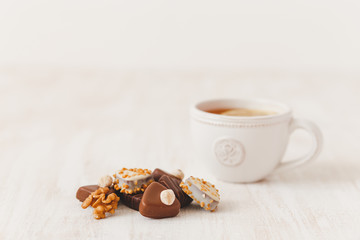 Chocolate candy with nuts and cup of hot tea with lemon on white wooden table, selective focus.