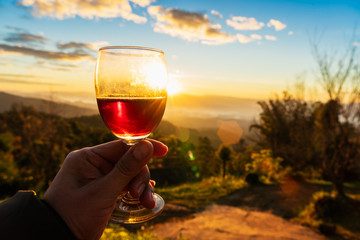 Man's hand holding glass of wine on sunset background.