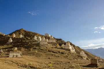 ancient white Tibetan Buddhist temples stupas on the slope of a desert hill against the blue sky and mountain valley