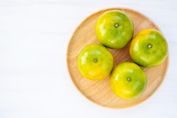 Green tangerine orange fruit on wooden plate, top view
