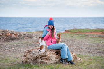 happy smiling beautiful girl in hat and track suit sitting on stone with two chihuahua small dogs...