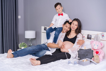 Obraz na płótnie Canvas happy family concept, pregnant mother, father and son on the bed