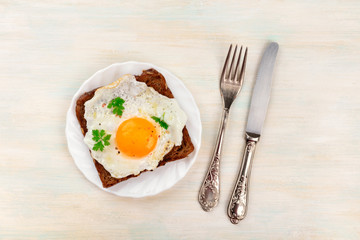 An overhead photo of an egg cooked sunny side up on a toast with a fork, knife and copy space