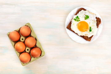An overhead photo of an egg cooked sunny side up on a toast and a carton of eggs, with a place for text