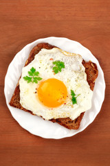 An egg cooked sunny side up on a toast, shot from above on a dark rustic wooden background with a place for text