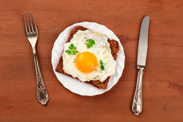 An egg cooked sunny side up on a toast with vintage cutlery, shot from the top on a dark rustic background with copy space