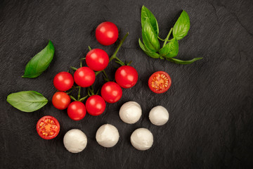 Naklejka na ściany i meble Mozzarella cheese, cherry tomatoes and fresh basil leaves, shot from the top on a black background, Italian cuisine ingredients with a place for text