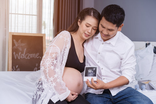 happy pregnant woman and her husband holding ultrasound scan photo on bed