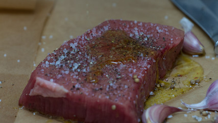 Extreme Close Up view of a Hand Seasoning Cooked piece of Meat in a Bright Light. Chef Accompanying Steak with Garlic, Rosemary, Pepper, Salt. Delicious, Modern Cuisine, Exclusive Recipe. 