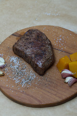 Extreme Close Up view of a Hand Seasoning Cooked piece of Meat in a Bright Light. Chef Accompanying Steak with Garlic, Rosemary, Pepper, Salt. Delicious, Modern Cuisine, Exclusive Recipe. 