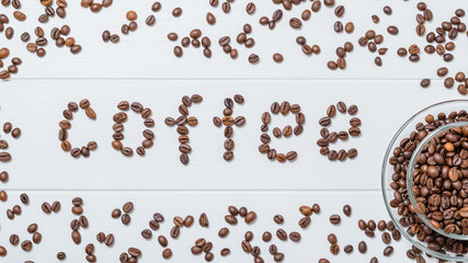 Scattered on a white table coffee beans and coffee inscription. The view from the top. Grains for the preparation of the popular drink.