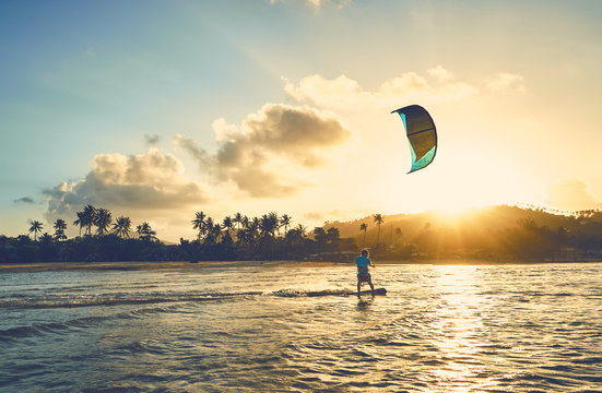 A young man is riding a kite-surf on the sea lagoon against the backdrop of sunset and palm trees