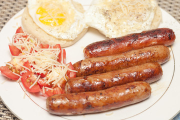 Fried rustic sausage links with sunny side up eggs with tomato and shreded aged cheese salad