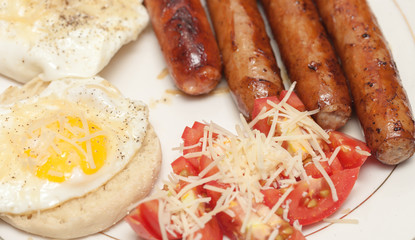 Fried rustic sausage links with sunny side up eggs with tomato and shreded aged cheese salad