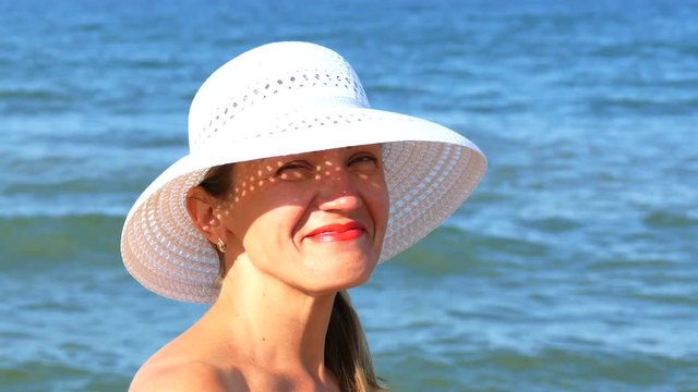    4K. Pretty woman in white hat put glasses, standing near ocean waves
