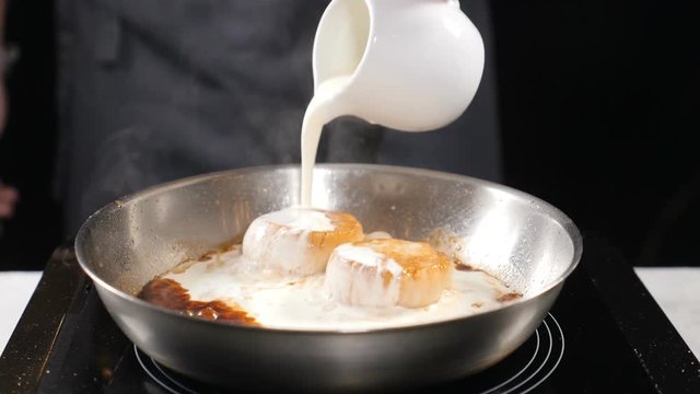 Cooking seafood. healthy food concept. Chef in gloves cooking scallops pouring cream dressing in slow motion. hd