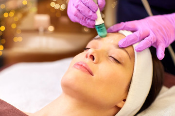 Obraz na płótnie Canvas people, beauty, cosmetology, exfoliation and technology concept - beautiful young woman having microdermabrasion facial treatment with crystals in spa