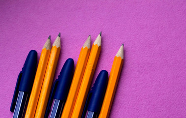 A group of simple orange pencils with blue pens close-up on a pink background