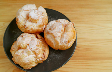 Top View of Three Choux a la Creme Pastries or French Cream Puffs on a Black Plate Served on Wooden Table