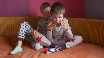 Funny kids lay on sofa to play computer games on smartphone. Parents gave the children a new phone for Christmas. Modern children are well aware of latest technology. Brothers are happy together