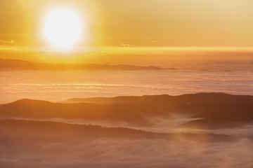 Fototapeta na wymiar Beautiful sunset over a valley filled by fog with mountains and hills