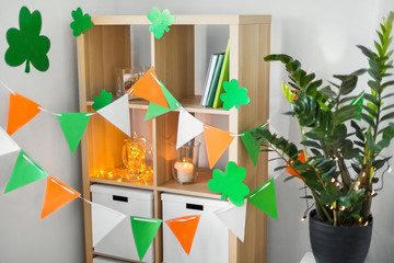 st patricks day, holidays and interior concept - close up of bookcase decorated by festive garland and shamrock for home party