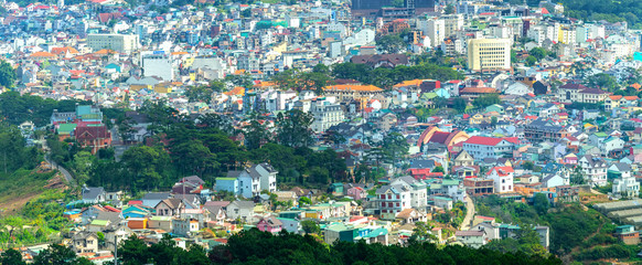 The panorama of Da Lat city is seen from above with the intertwined house architecture with forest mountains showing the urban development in the most tourist city in Vietnam