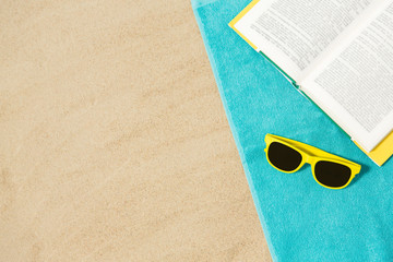 vacation, travel and summer holidays concept - yellow sunglasses and book on blue beach towel on sand - Powered by Adobe