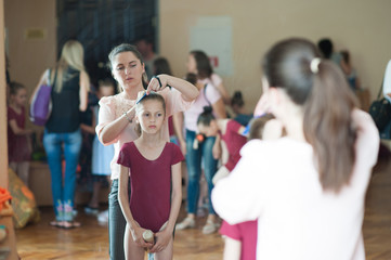 young caucasian mother corrects her ballerina dancer little slim daughter's hair before concert show