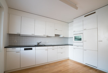 modern bright kitchen in an empty refurbished apartment with black granite work surface and wooden parquet floor