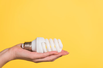 Fototapeta na wymiar cropped view of woman holding fluorescent lamp isolated on yellow, energy efficiency concept