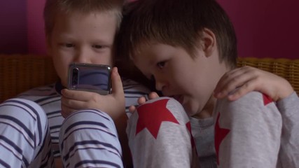 Funny kids lay on sofa to play computer games on smartphone. Parents gave the children a new phone for Christmas. Modern children are well aware of latest technology. Brothers are happy together