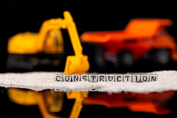 Toy construction vehicles and sand with the word construction on beads reflected on black background