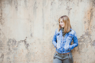 Young beautiful woman with denim jacket standing on a rusted wall