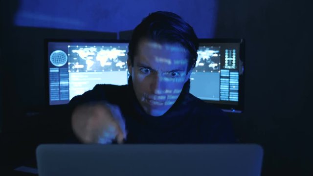 Portrait of Angry Hacker Programmer screams and shows aggression while working at the computer. Stress in the workplace.